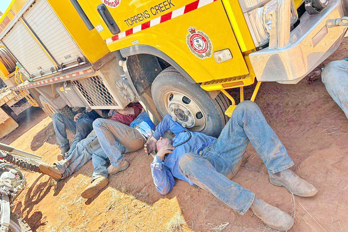 Firefighting volunteers take a much-deserved break in the shade created by a tanker from the Torrens Creek and Prairie Rural Fire Brigade.