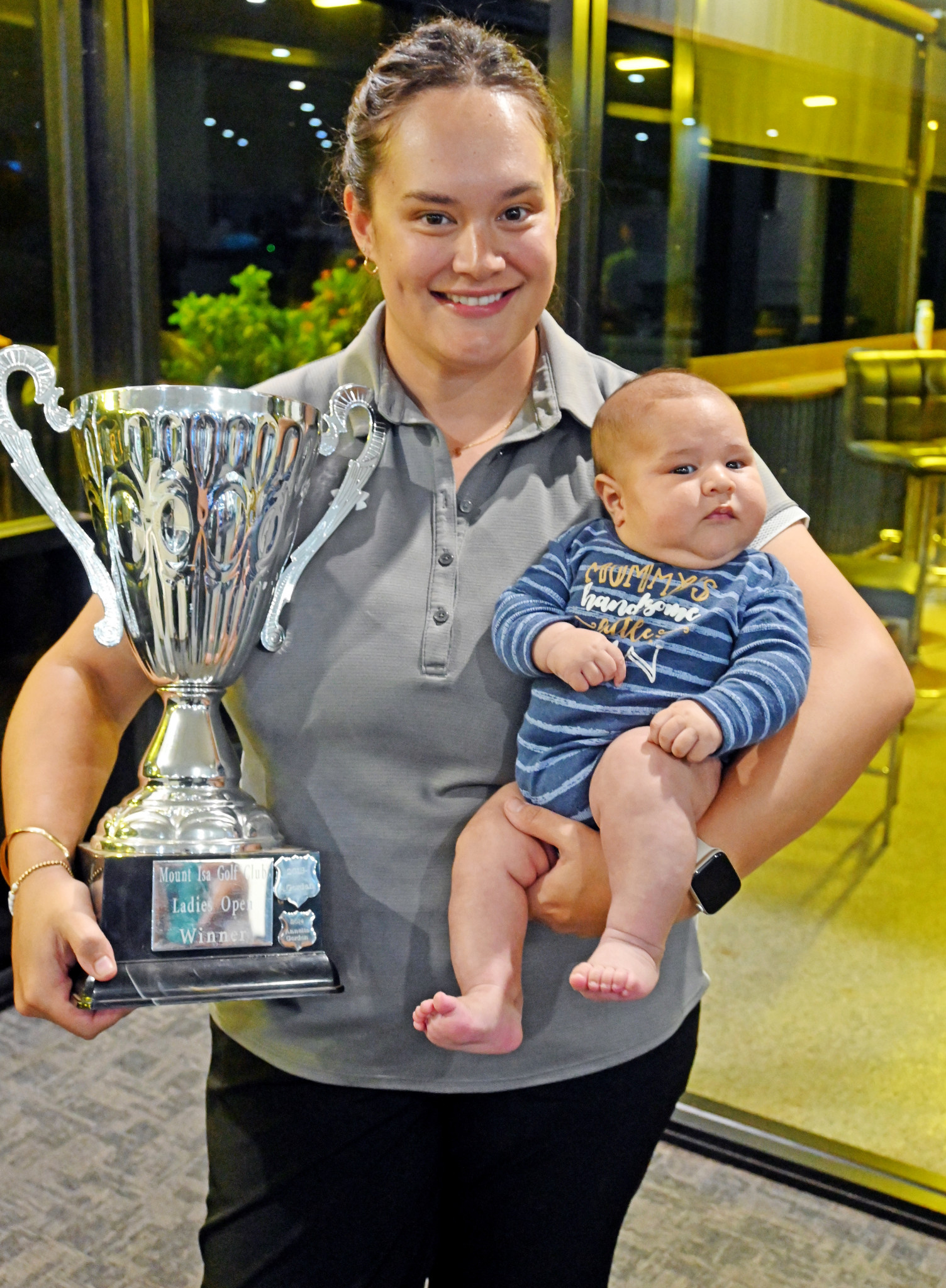 New mum and City of Mount Isa Open women’s champion Kate Chadwick with two prized possessions, her son Eli and the winning trophy.