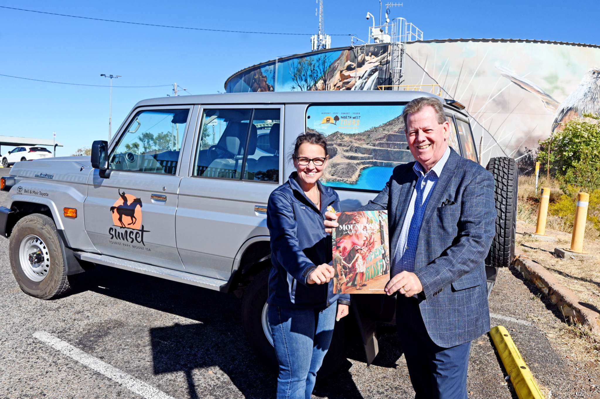 Sunset Tourist Park’s Kylie Rixon holds a copy of the Mount Isa Visitor’s Guide with Lee Pulman from Bell and Moir Toyota, who has donated a Toyota LandCruiser 70 Series so that Kylie can venture out to promote Mount Isa.